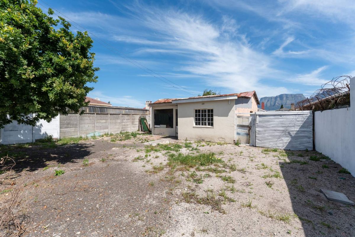 Rear exterior view of the property featuring a small structure with a corrugated roof, enclosed by concrete boundary walls and security fencing.