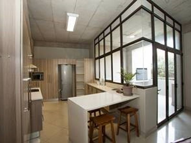 Modern kitchen featuring light wood cabinetry, stone countertops, a breakfast bar, and a distinctive glass partition wall overlooking an adjacent outdoor area.