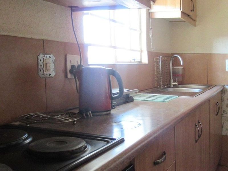 A compact kitchen featuring built-in cabinetry, a laminate countertop, a stainless steel sink, and an integrated electric hob with tiled splashback.
