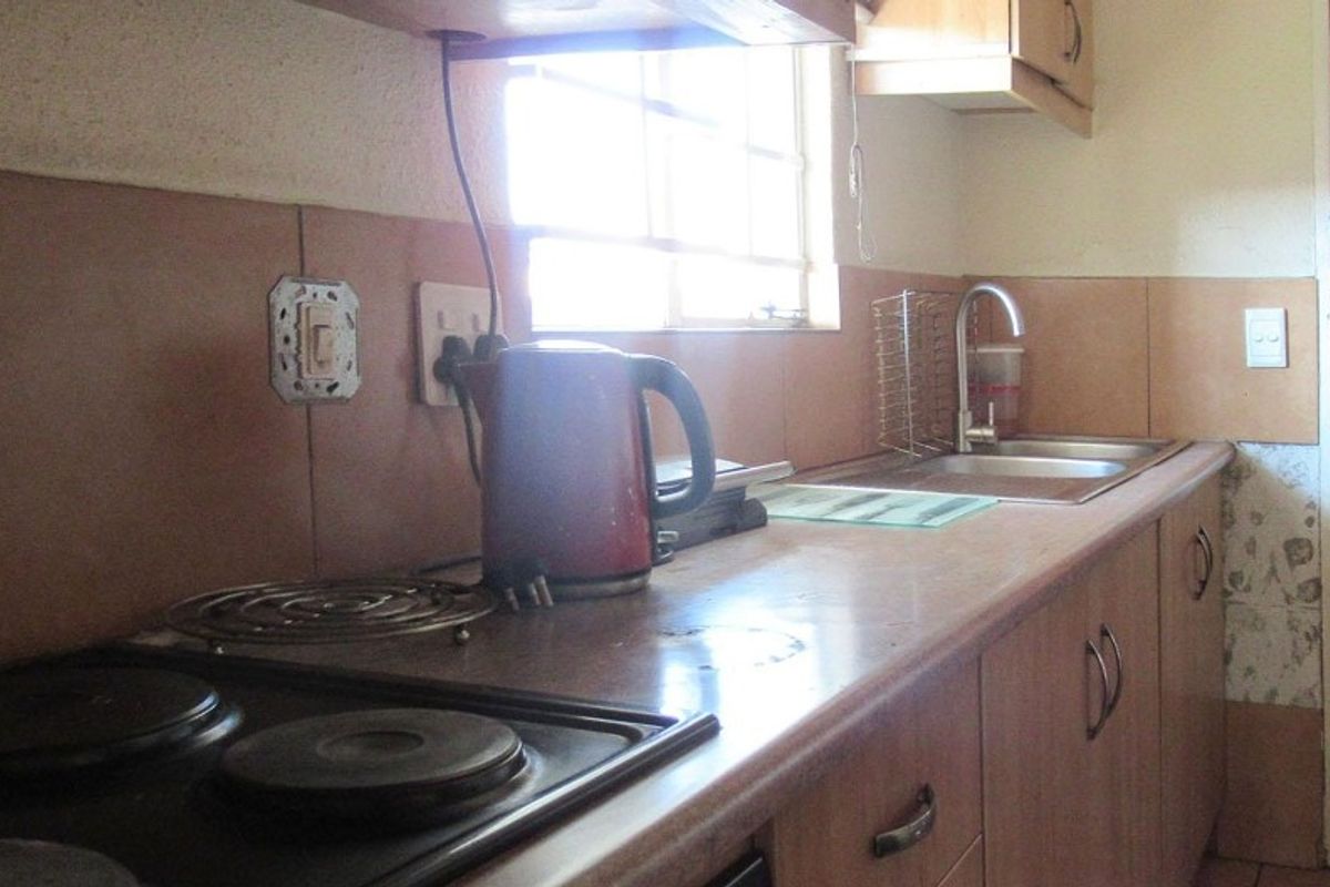 A compact kitchen featuring built-in cabinetry, a laminate countertop, a stainless steel sink, and an integrated electric hob with tiled splashback.