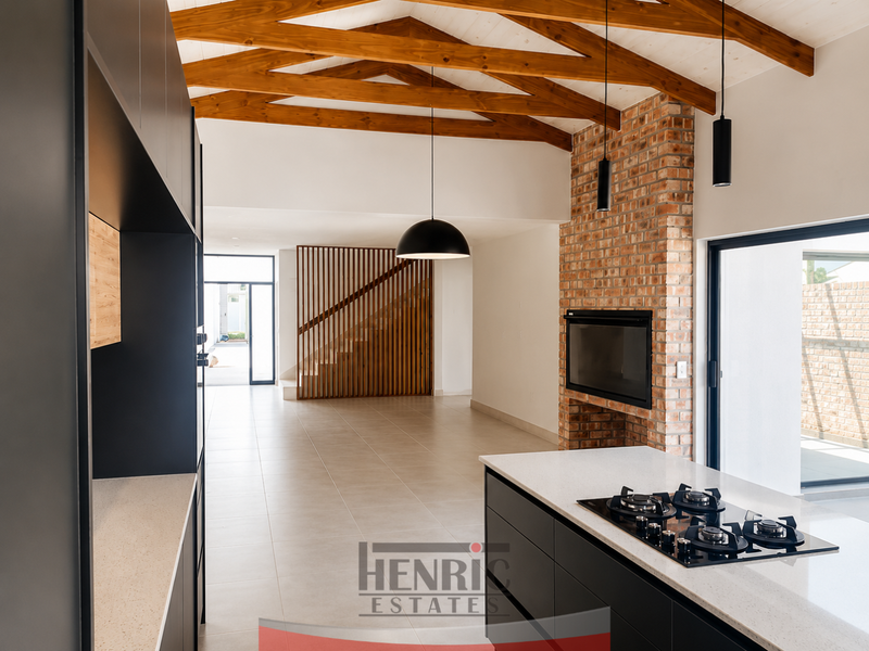 Modern open-plan living area featuring exposed timber trusses, a brick fireplace, and a sleek kitchen with a central island and gas hob.