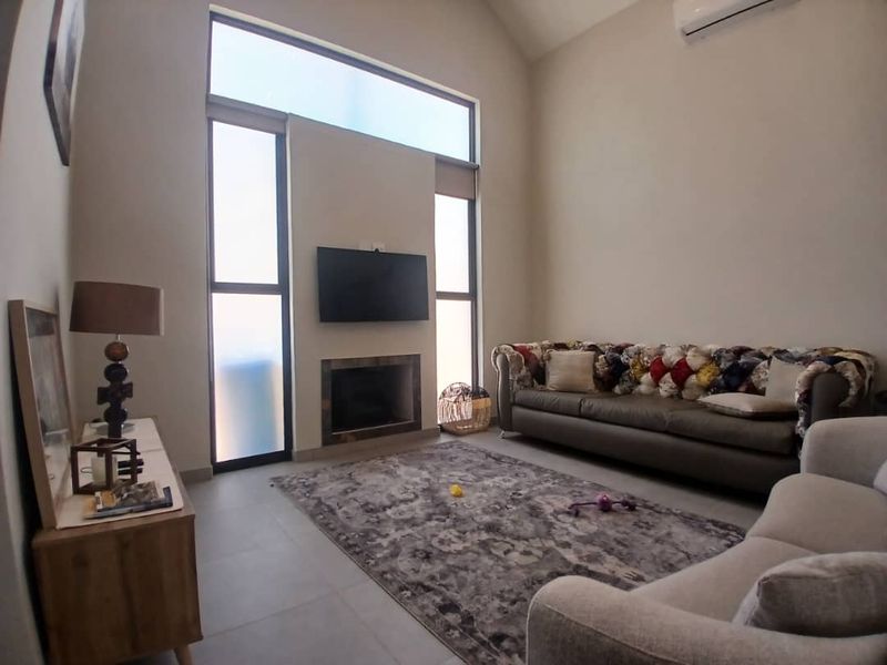 Spacious living room featuring high-vaulted ceilings, large vertical windows for natural light, a built-in fireplace, and a wall-mounted air conditioning unit.