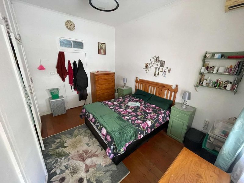 A functional bedroom featuring timber flooring, a built-in wardrobe, and a transom window above the door, providing a practical living space.