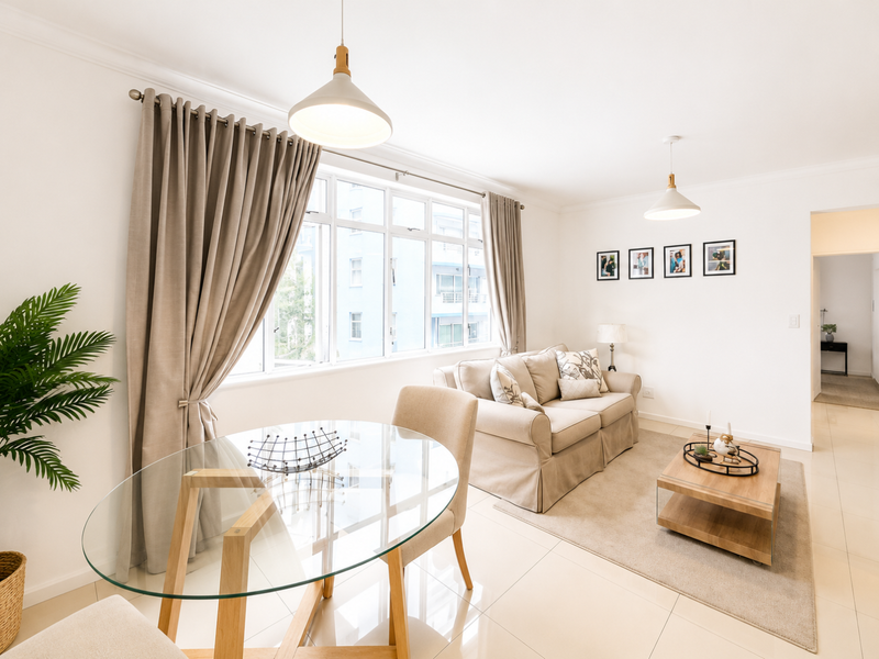 A bright and well-maintained open-plan living and dining area featuring neutral tiled flooring, modern pendant lighting, and large windows allowing for ample natural light.