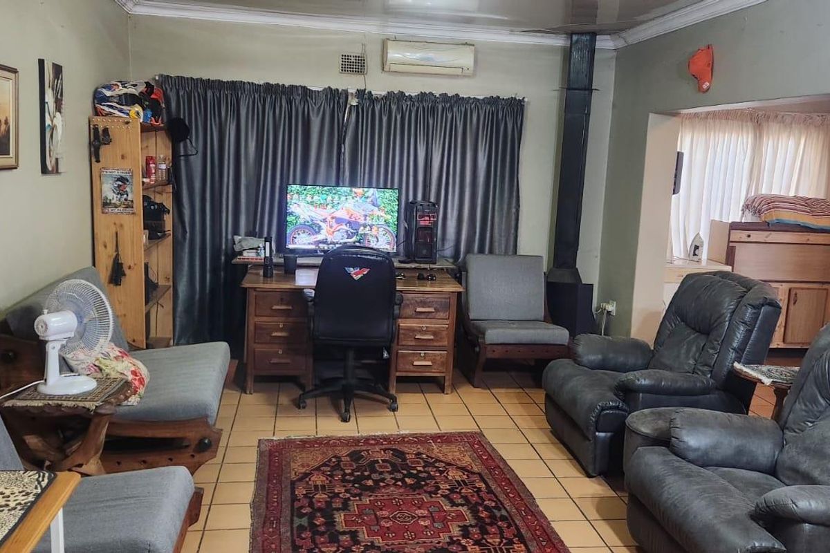 A living room featuring tiled flooring, a wood-burning stove, and a wall-mounted air conditioning unit, offering a functional space with potential for cosmetic updates.