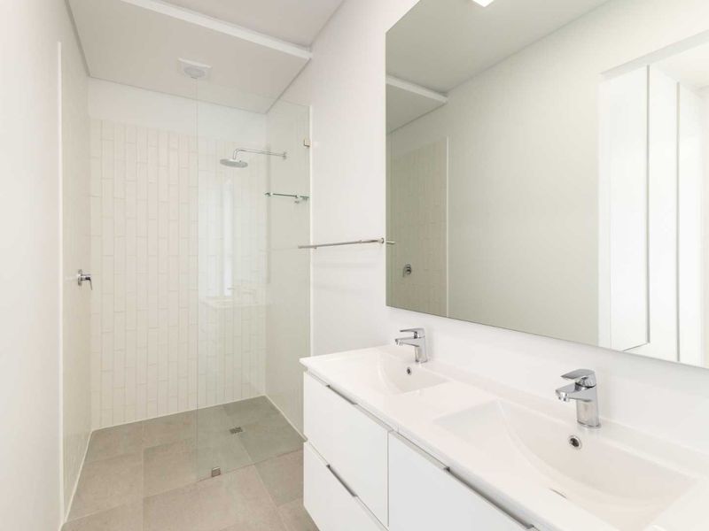 Modern bathroom featuring a double vanity with integrated sinks, large wall mirror, and a spacious walk-in shower with a glass screen and subway tiling.