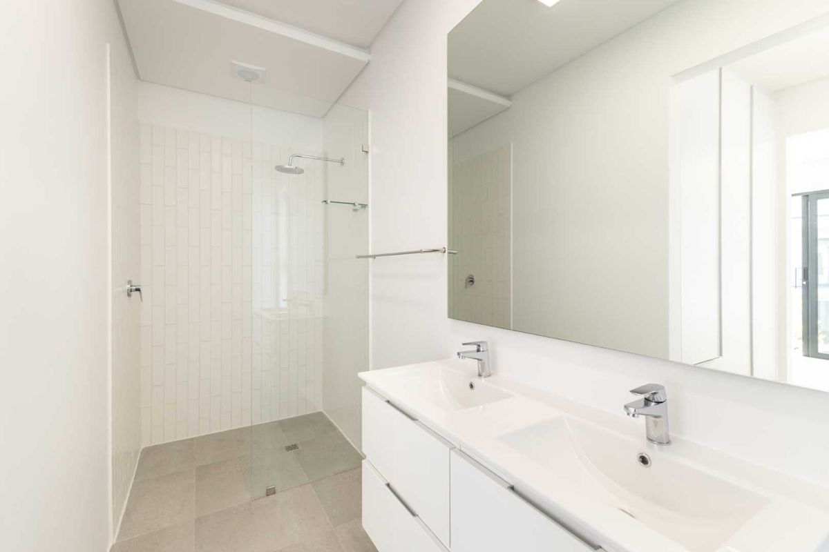 Modern bathroom featuring a double vanity with integrated sinks, large wall mirror, and a spacious walk-in shower with a glass screen and subway tiling.