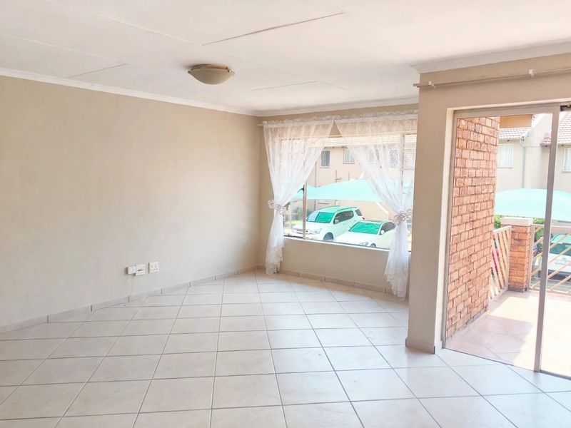 A bright, empty living area featuring tiled floors, a sliding door leading to a balcony, and neutral wall finishes.