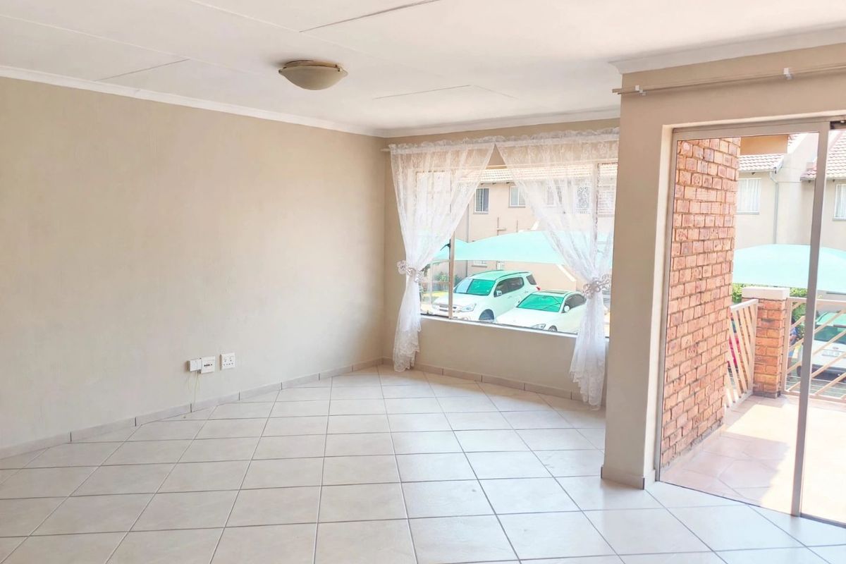 A bright, empty living area featuring tiled floors, a sliding door leading to a balcony, and neutral wall finishes.