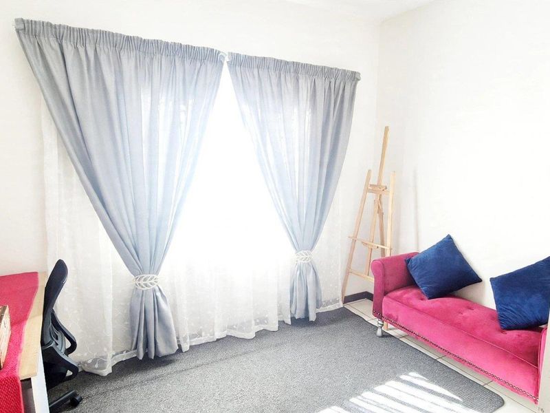 A bedroom featuring neutral walls, carpeted flooring, and a window dressed with curtains, offering a functional and well-lit living space.