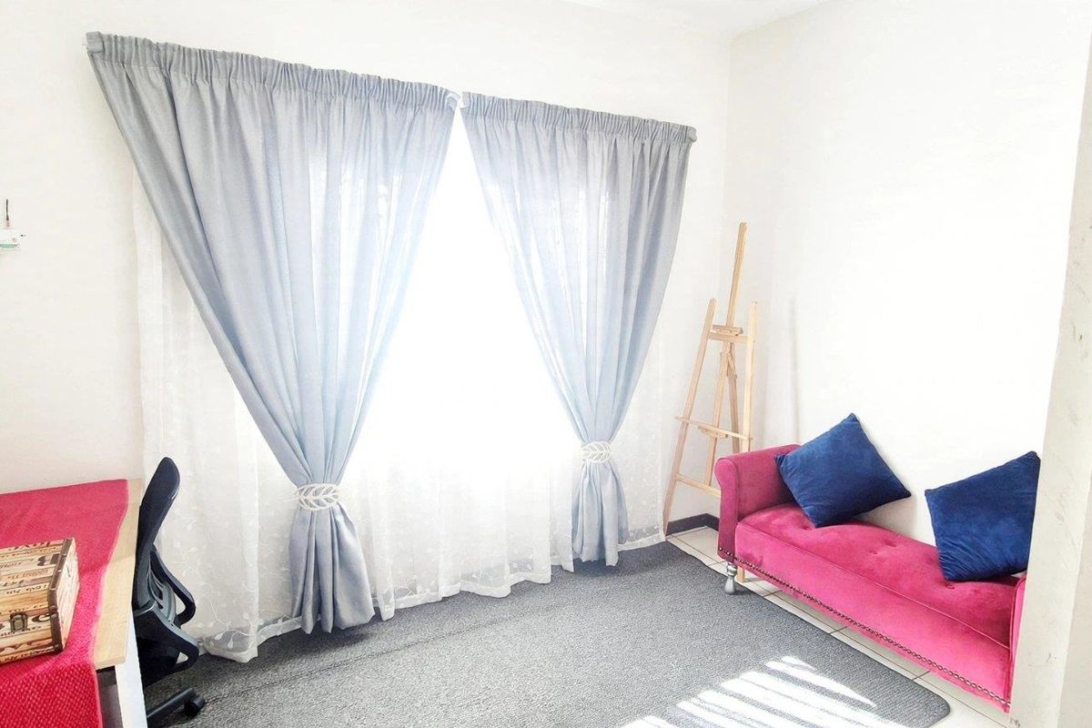 A bedroom featuring neutral walls, carpeted flooring, and a window dressed with curtains, offering a functional and well-lit living space.
