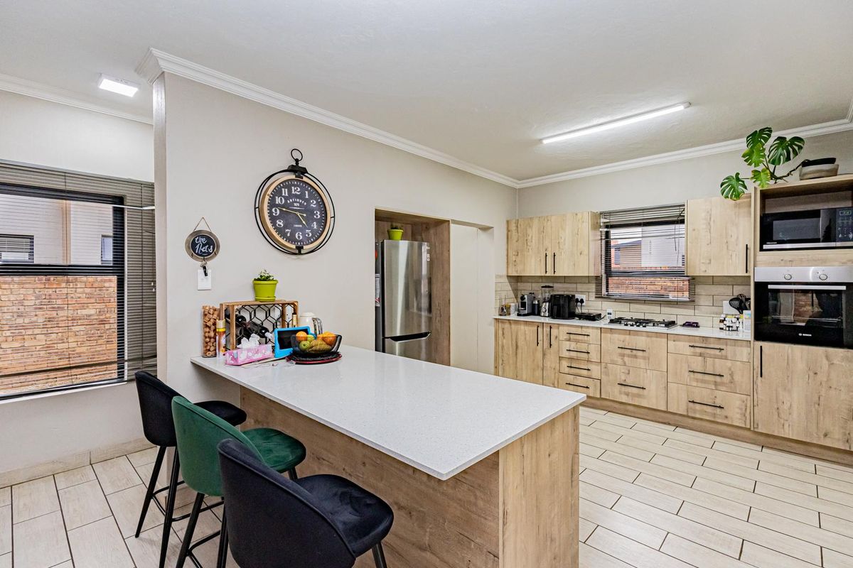 Modern kitchen featuring light wood-finish cabinetry, stone countertops, a central island, built-in oven, gas hob, and tiled flooring.