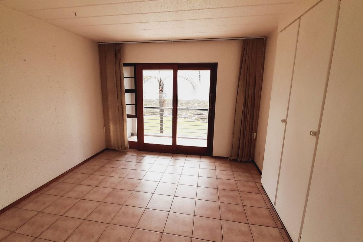 An empty bedroom featuring tiled flooring, built-in cupboards, and a sliding glass door providing access to a balcony with outdoor views.