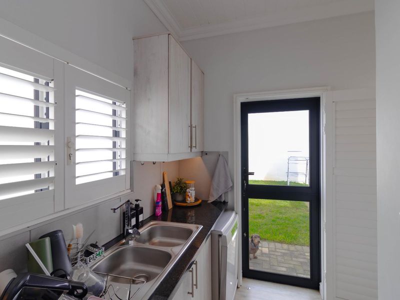 A functional scullery featuring granite countertops, a double bowl stainless steel sink, built-in cabinetry, and direct access to the rear garden.