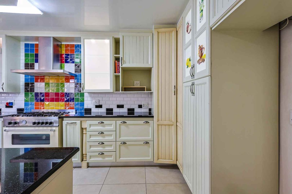 A kitchen featuring cream-colored cabinetry, a black granite countertop, and a vibrant multi-colored tiled backsplash with a built-in oven and extractor fan.
