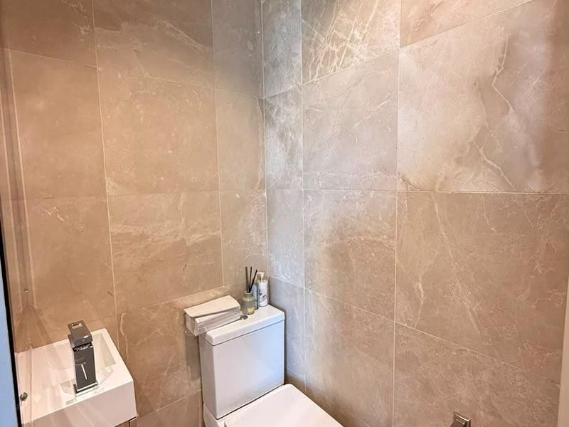 A compact modern bathroom featuring floor-to-ceiling beige marble-look tiles, a wall-mounted vanity, and a contemporary toilet.