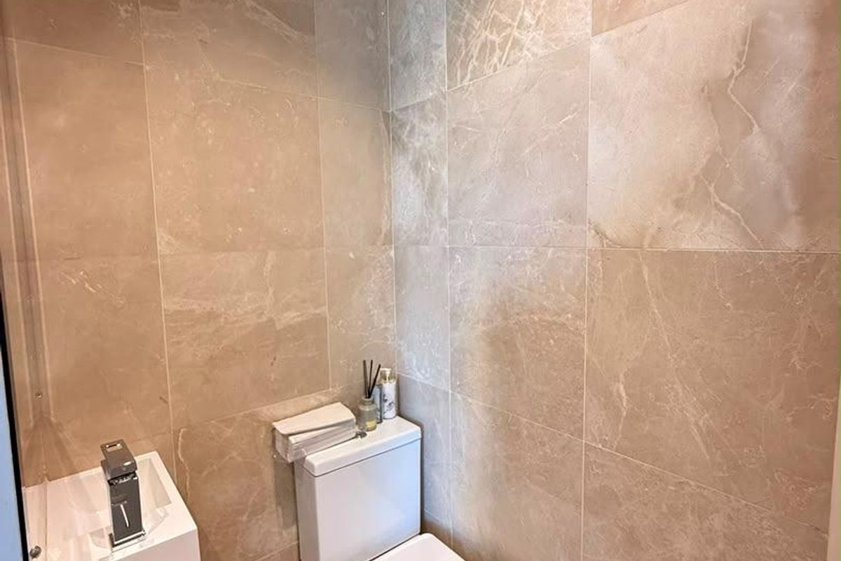 A compact modern bathroom featuring floor-to-ceiling beige marble-look tiles, a wall-mounted vanity, and a contemporary toilet.