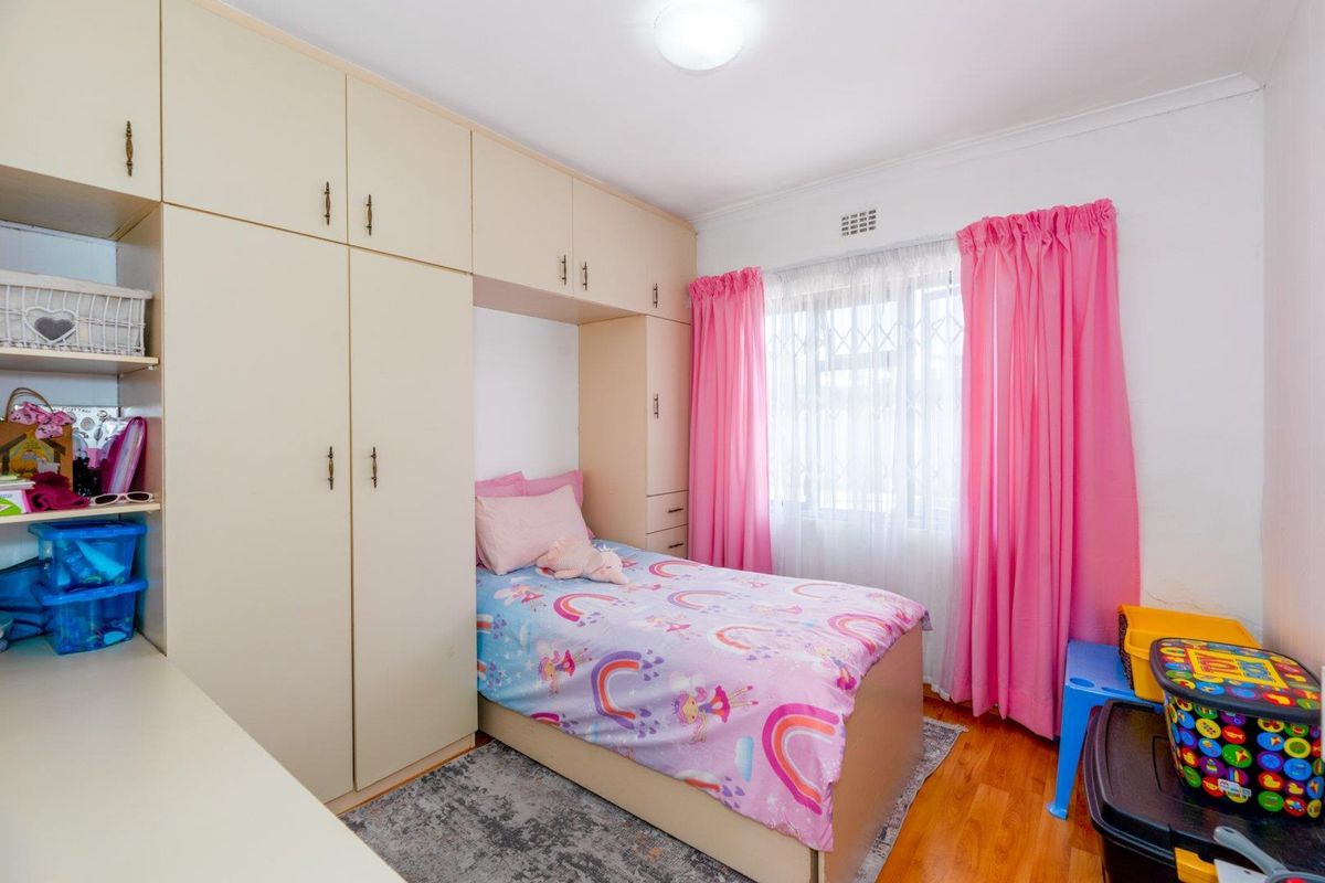 A bedroom featuring built-in cupboards, laminate flooring, and a window fitted with a security gate.