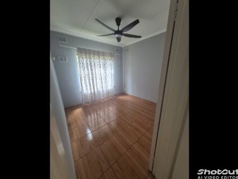 A vacant bedroom featuring wood-look tiled flooring, a ceiling fan, and neutral wall finishes, offering a clean and versatile space.