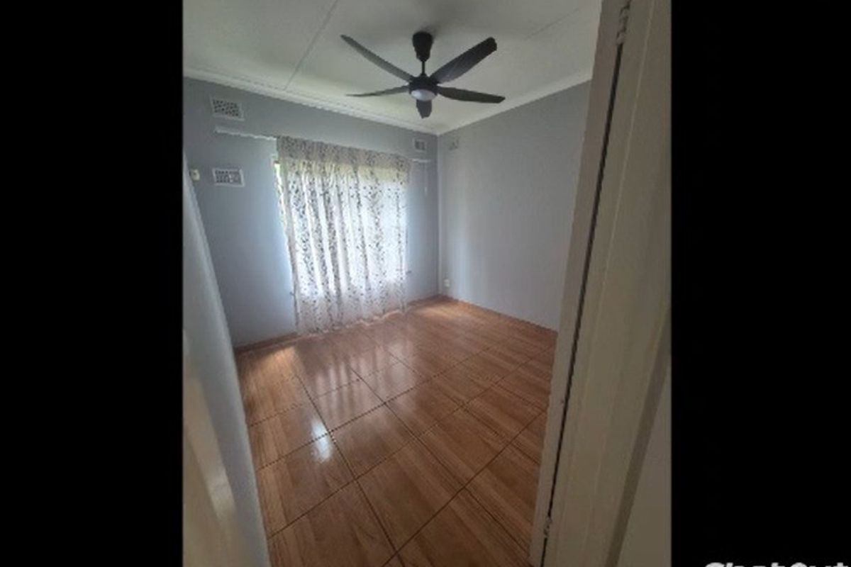 A vacant bedroom featuring wood-look tiled flooring, a ceiling fan, and neutral wall finishes, offering a clean and versatile space.