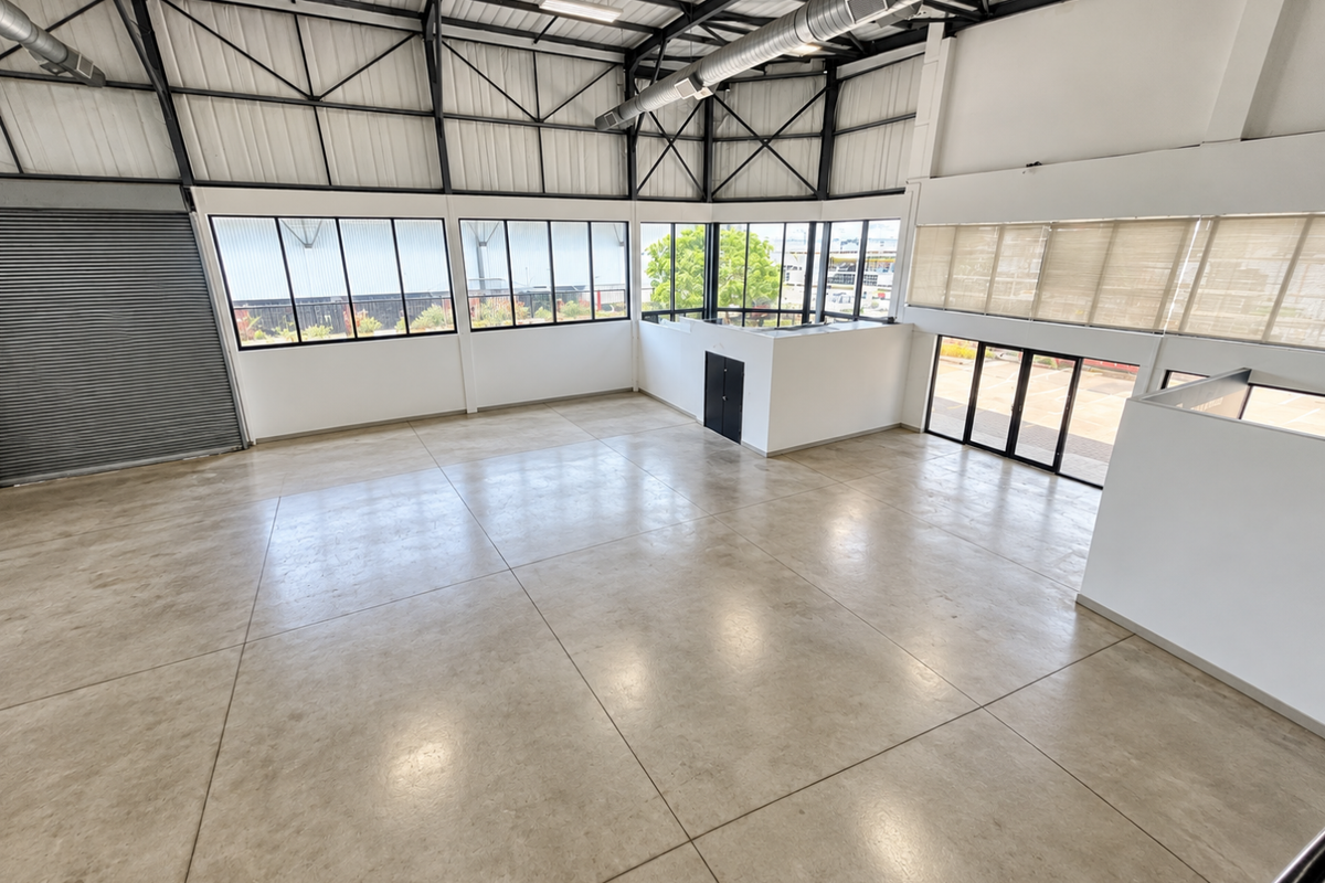 Spacious industrial-style open-plan unit featuring high ceilings with exposed steel trusses, polished concrete floors, and large windows providing ample natural light.