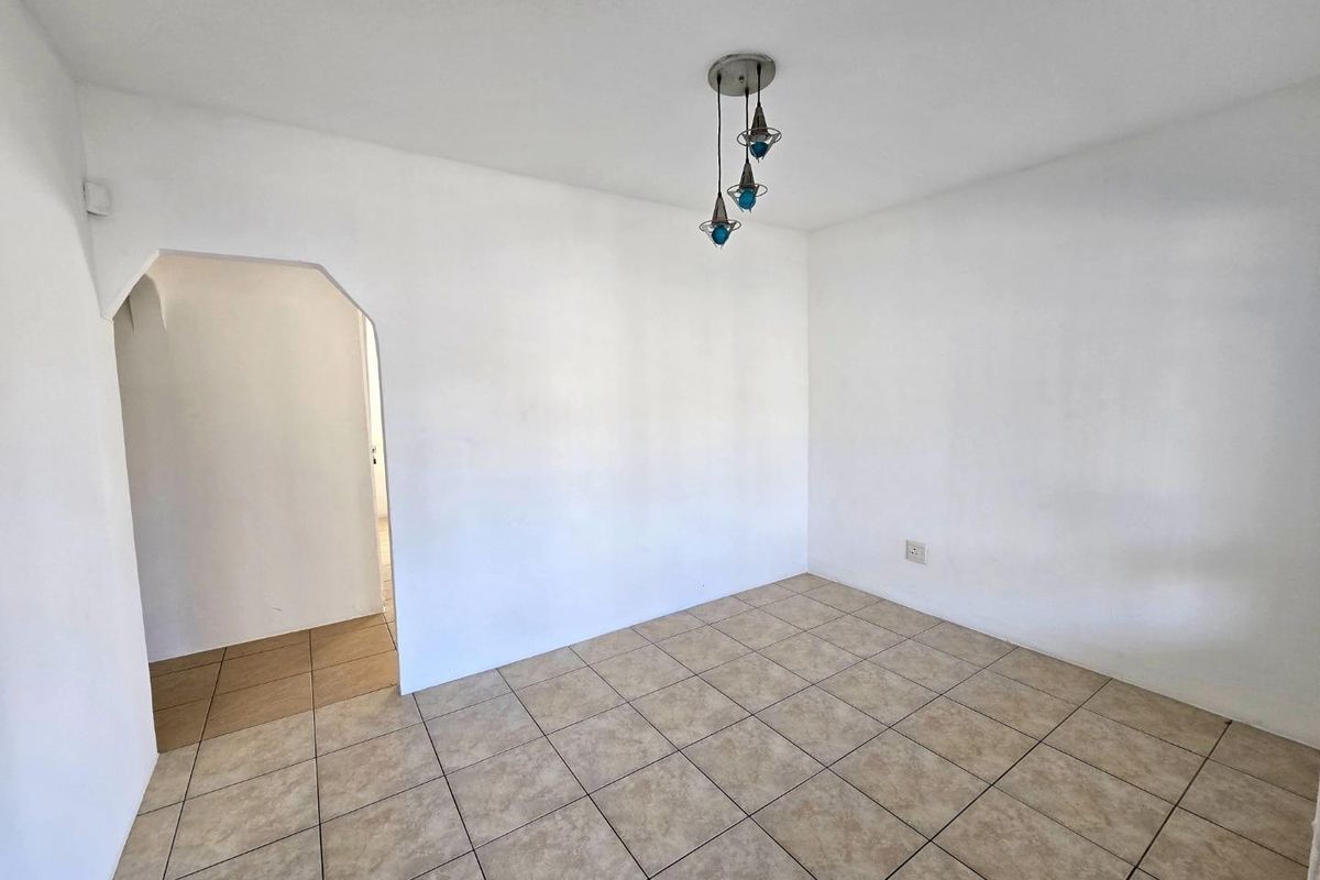 An empty living room featuring neutral ceramic floor tiles, a distinctive arched doorway, and a modern pendant light fixture.