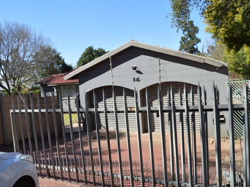 Front view of the property featuring a double garage, paved driveway, and secure perimeter fencing with electric security wires.