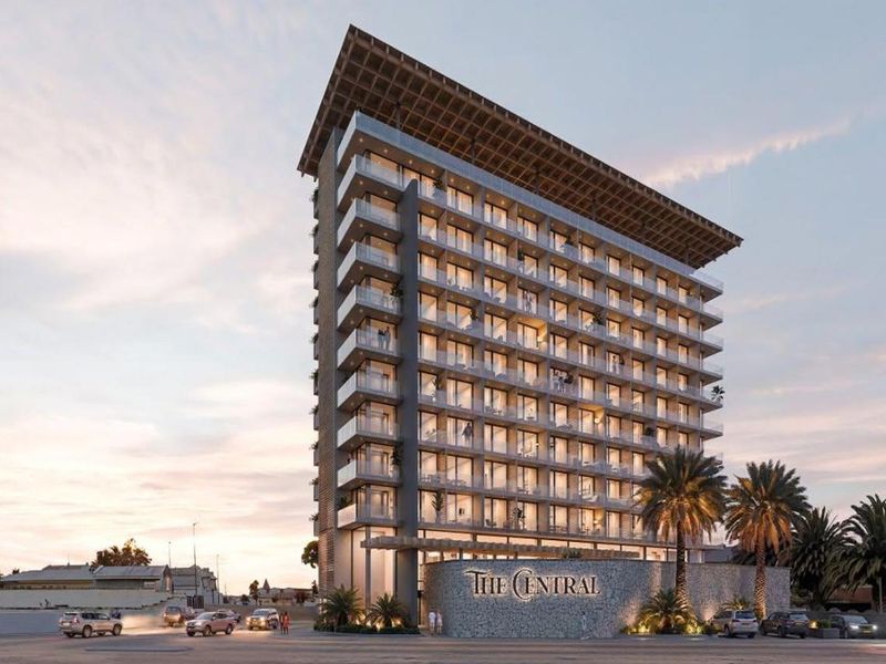 A modern high-rise hotel building featuring glass balconies, stone facade detailing, and a prominent entrance area at street level.