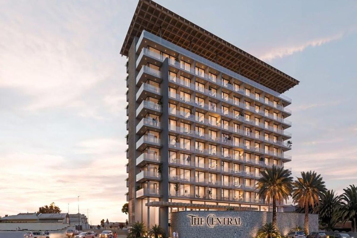 A modern high-rise hotel building featuring glass balconies, stone facade detailing, and a prominent entrance area at street level.