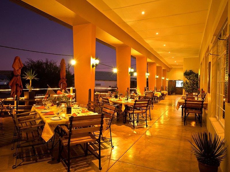 A spacious covered outdoor patio area featuring concrete flooring, warm recessed lighting, and wall-mounted sconces, ideal for evening dining and entertainment.