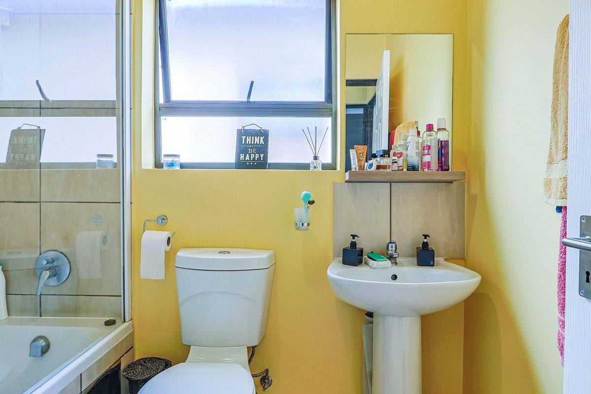 A functional bathroom featuring a pedestal sink, a toilet, and a shower-over-bath combination with tiled surrounds and a window for natural light.