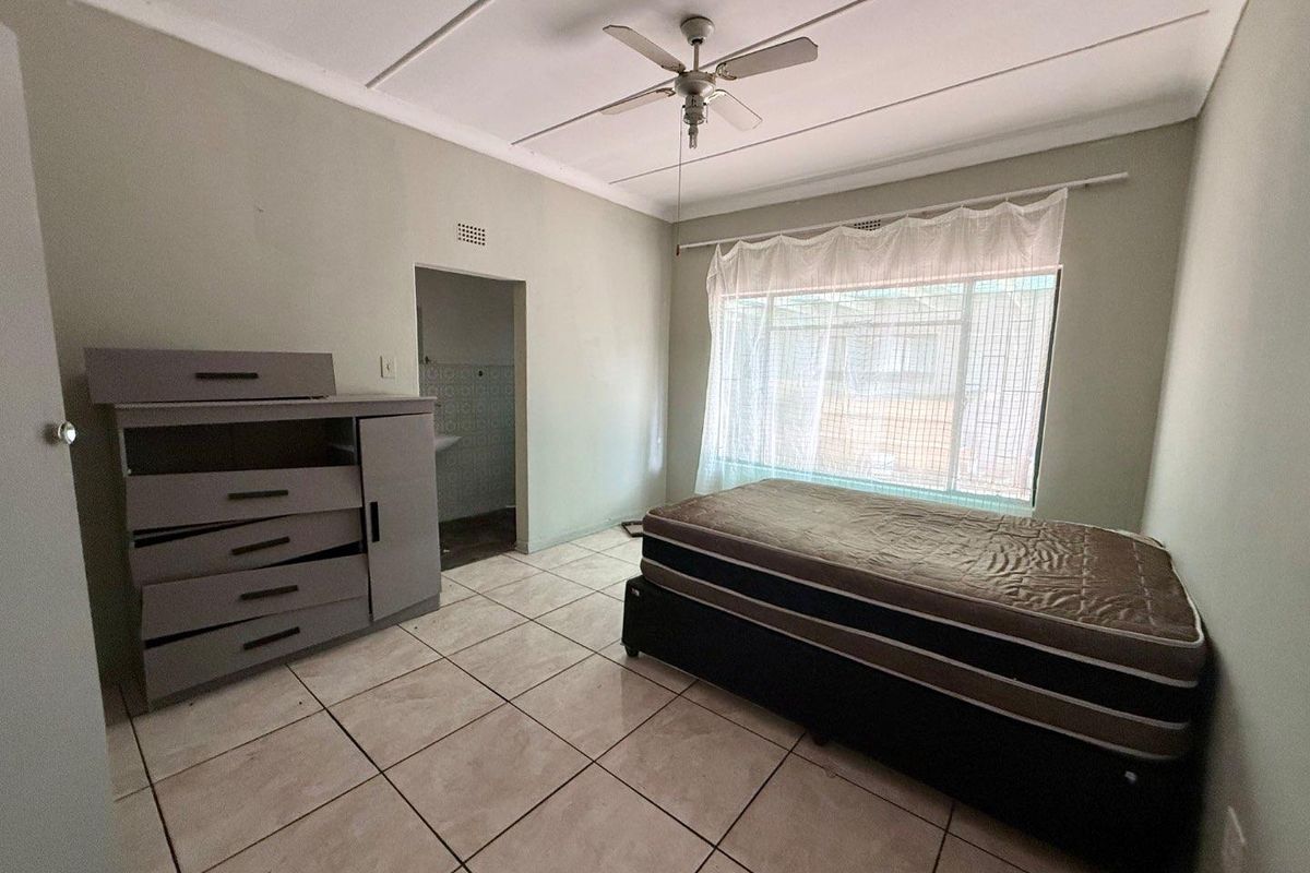 A bedroom featuring tiled flooring, a ceiling fan, and an adjoining doorway leading to an en-suite bathroom area.