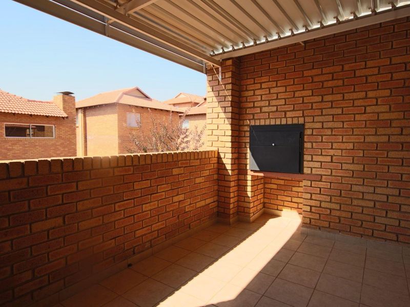 A covered balcony featuring exposed brick walls, tiled flooring, and a built-in braai, offering a functional outdoor entertainment space.