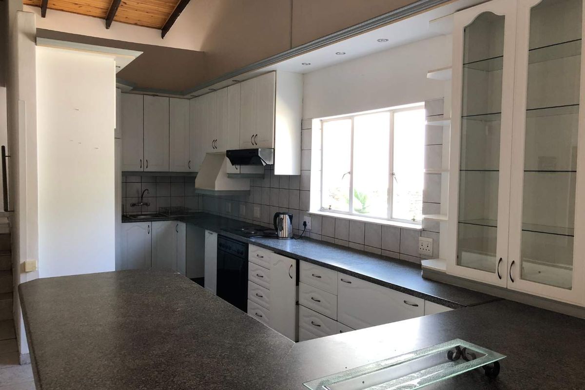 A spacious kitchen featuring white cabinetry, dark laminate countertops, a double sink, and a high vaulted ceiling with exposed timber beams.