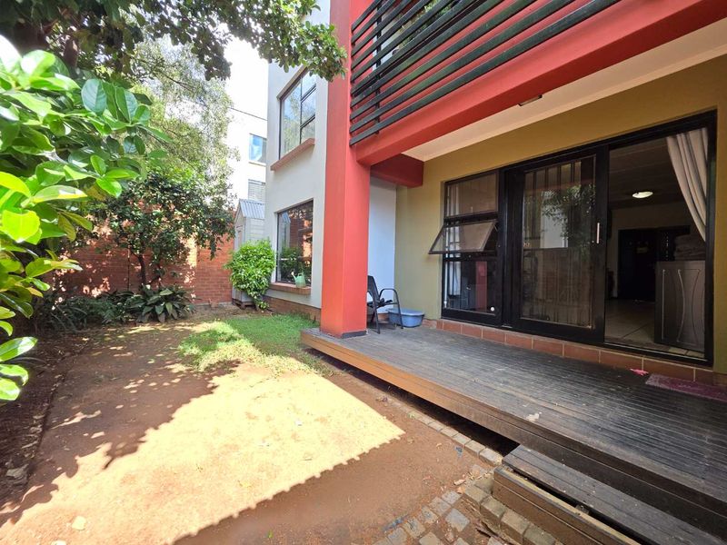 Rear view of the apartment featuring a timber deck, sliding glass doors, and a private garden area with a brick boundary wall.
