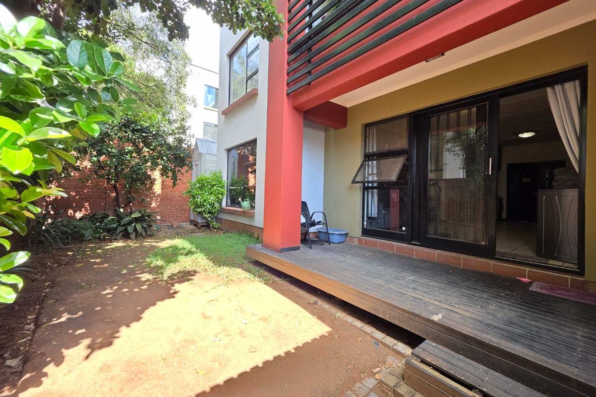 Rear view of the apartment featuring a timber deck, sliding glass doors, and a private garden area with a brick boundary wall.