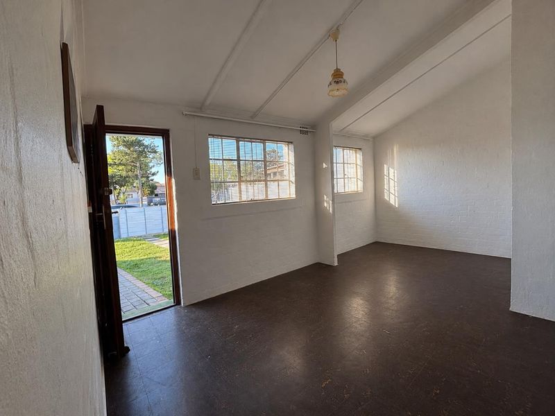 A bright, empty living room featuring painted brick walls, exposed beam ceilings, and vinyl flooring with direct access to the garden.