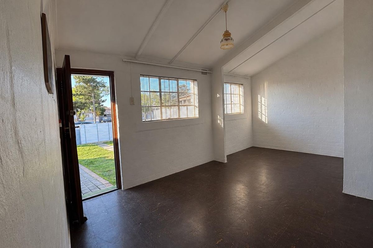 A bright, empty living room featuring painted brick walls, exposed beam ceilings, and vinyl flooring with direct access to the garden.