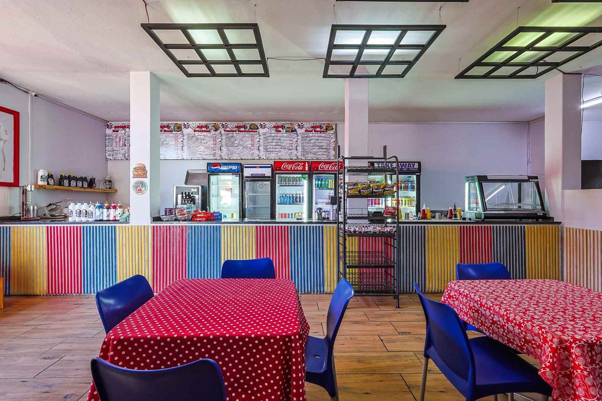Open-plan commercial dining area featuring a service counter, tiled flooring, and suspended grid lighting, suitable for a cafe or restaurant setup.