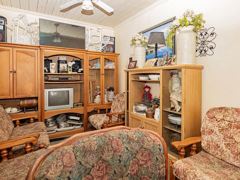 A living room featuring a ceiling fan and timber-look ceiling paneling, currently filled with dated cabinetry and furniture.