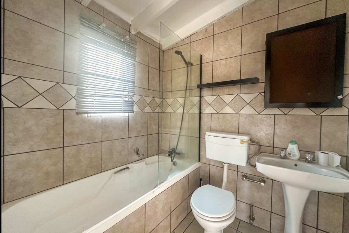 A functional bathroom featuring a bathtub with a glass shower screen, pedestal basin, and toilet, finished with neutral wall and floor tiling.