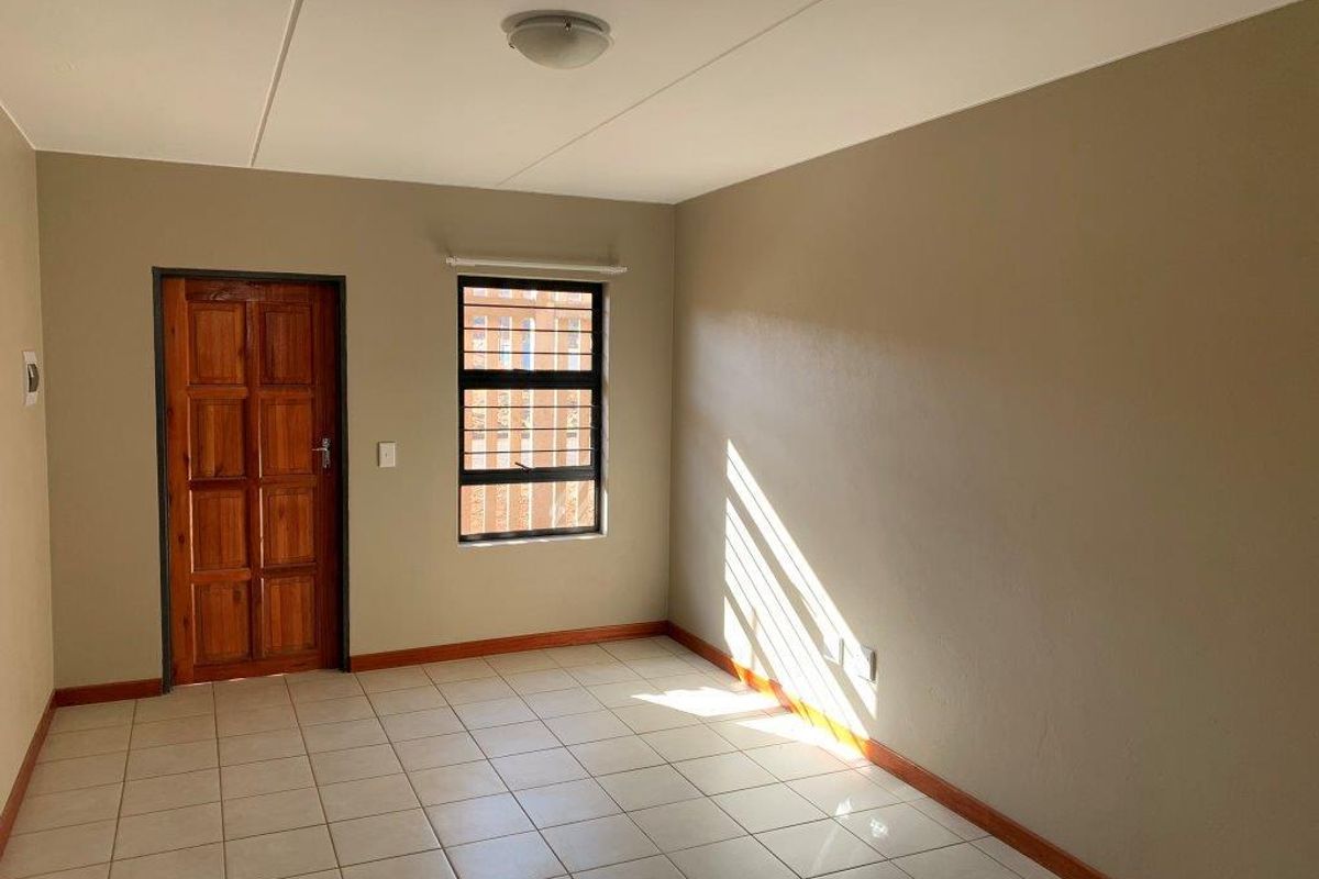 A bright, empty bedroom featuring neutral wall tones, tiled flooring, and a timber door, offering a clean canvas for personalization.