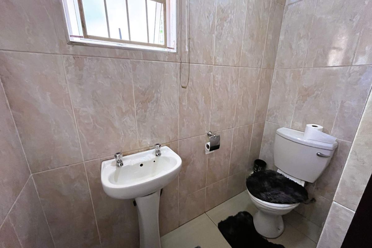 A compact bathroom featuring floor-to-ceiling wall tiles, a pedestal basin, and a standard toilet.