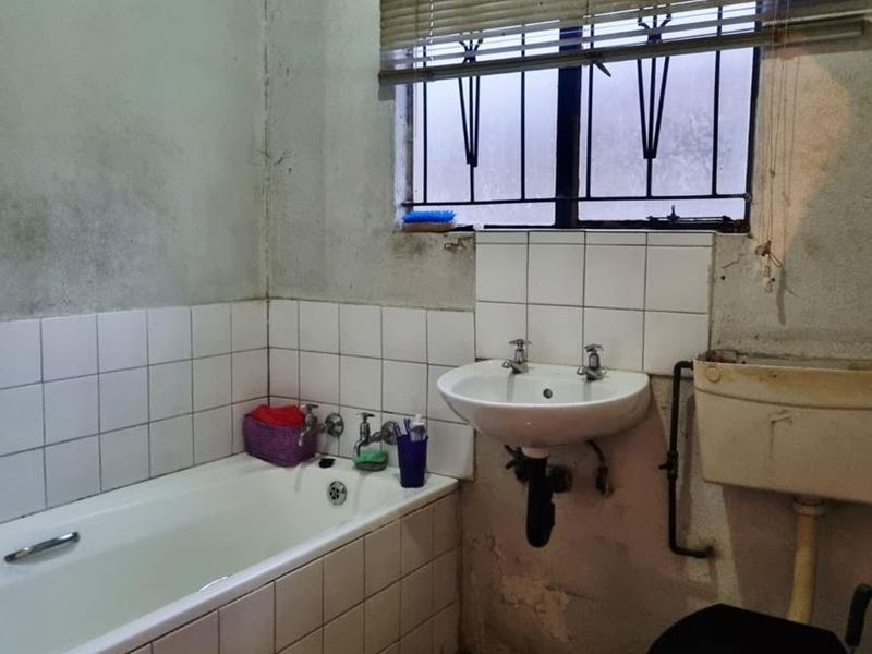 A dated bathroom featuring a bathtub, wall-mounted basin, and high-level cistern toilet, requiring significant renovation and cosmetic updates to improve its condition.