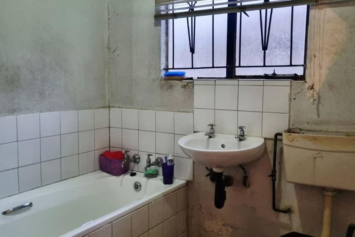 A dated bathroom featuring a bathtub, wall-mounted basin, and high-level cistern toilet, requiring significant renovation and cosmetic updates to improve its condition.