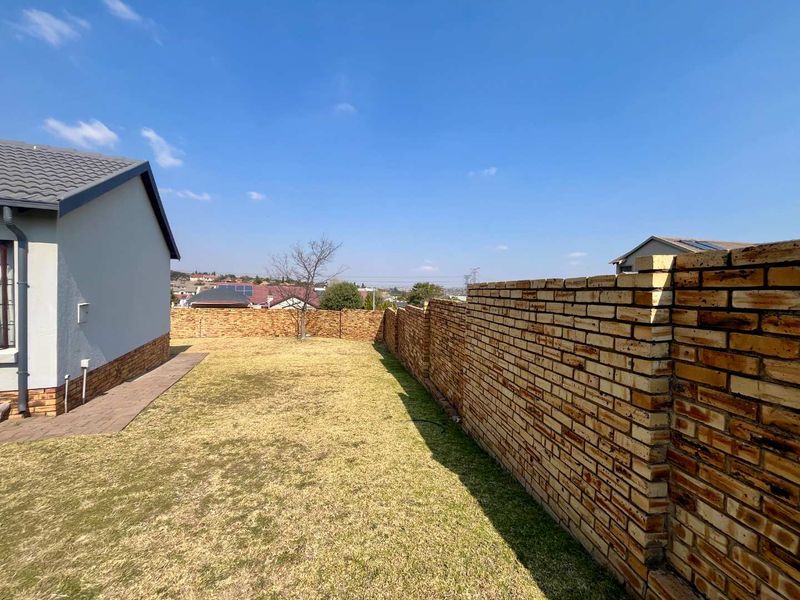 A private rear garden area featuring a well-maintained lawn, paved walkway, and a sturdy face brick boundary wall.