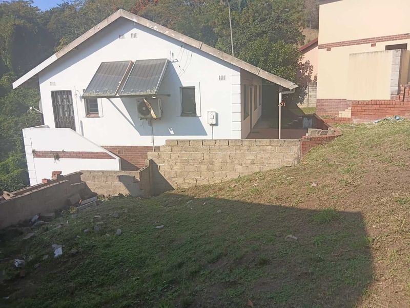 Rear view of the house featuring a solar water heater, external air conditioning unit, and a brick retaining wall in the backyard.