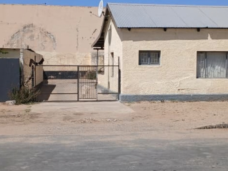 Front exterior view of a commercial property featuring a textured plaster facade, corrugated metal roof, and secure gated access.
