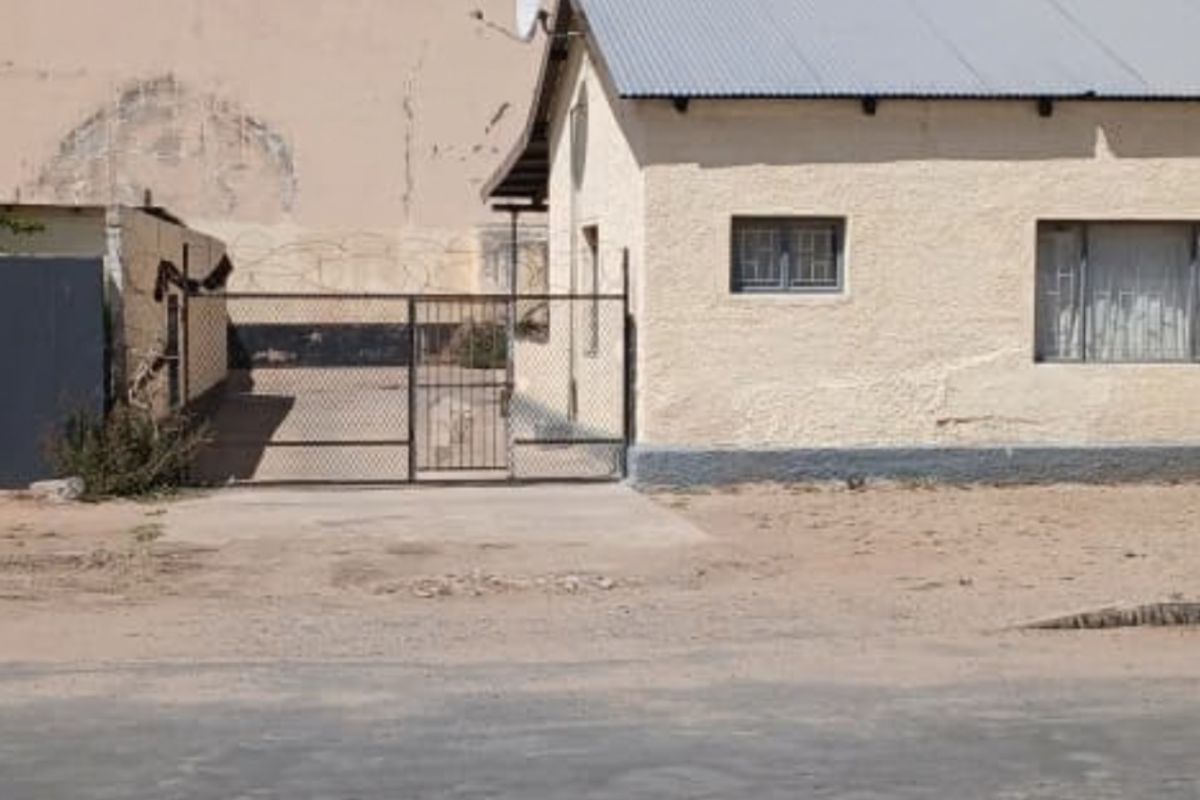 Front exterior view of a commercial property featuring a textured plaster facade, corrugated metal roof, and secure gated access.