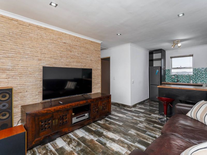 Open-plan living area featuring a textured stone feature wall, modern laminate flooring, and an integrated kitchen with a breakfast bar.